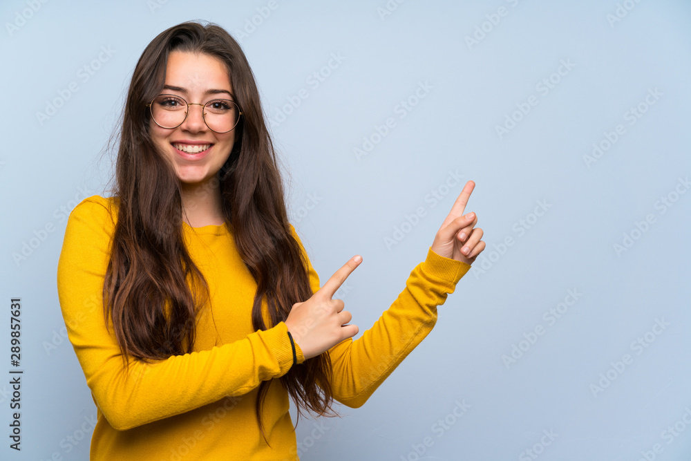 © luismolinero - Teenager girl over isolated blue wall pointing finger to the side