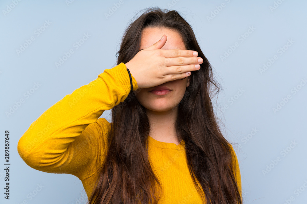Teenager girl over isolated blue wall covering eyes by hands Teenager girl over isolated blue wall covering eyes by hands