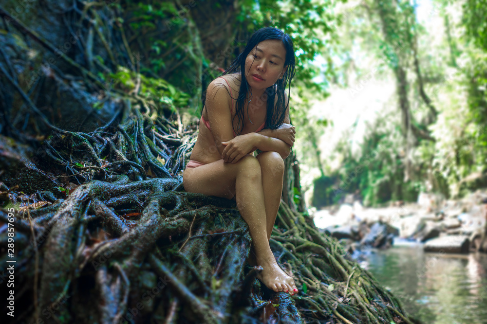 beautiful woman at tropical enchanted forest . Young attractive Asian Korean girl in bikini sitting on tree trunk at tropical paradise jungle with a mysterious and magical feeling beautiful woman at tropical enchanted forest . Young attractive Asian Korean girl in bikini sitting on tree trunk at tropical paradise jungle with a mysterious and magical feeling