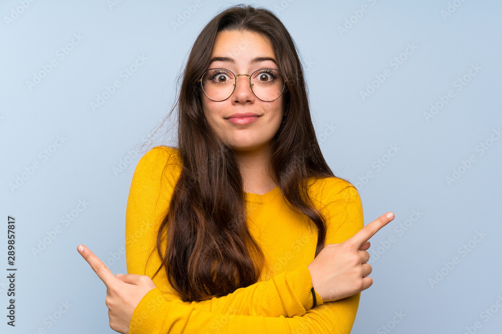 Teenager girl over isolated blue wall pointing to the laterals having doubts Teenager girl over isolated blue wall pointing to the laterals having doubts