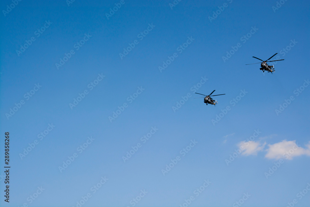 Two gray military helicopters fly in the blue sky. Demonstration of a peaceful flight. Day of the city. Memory. Air show Background with copy space for text. Two gray military helicopters fly in the blue sky. Demonstration of a peaceful flight. Day of the city. Memory. Air show Background with copy space for text.