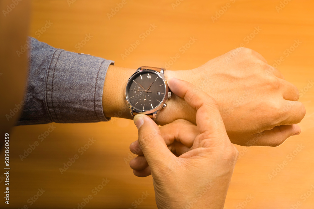 Soft light, Men's looking at his luxury watches brown leather strap that are worn in the hands, to checking or setting the time on his watch. on the brown wooden table background. Soft light, Men's looking at his luxury watches brown leather strap that are worn in the hands, to checking or setting the time on his watch. on the brown wooden table background.