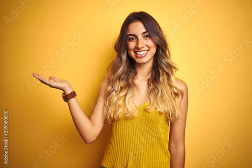 Young beautiful woman wearing t-shirt over yellow isolated background smiling cheerful presenting and pointing with palm of hand looking at the camera.