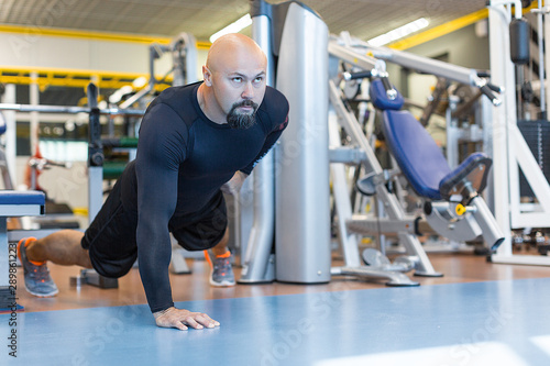Brutal bearded man doing push ups exercise with one hand in fitness gym.