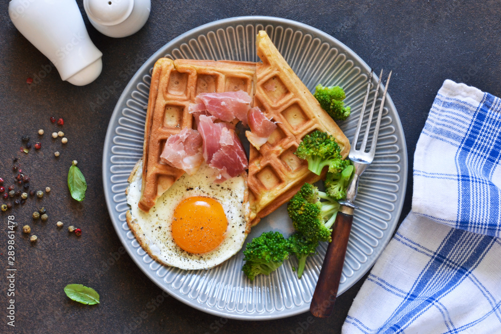 Belgian waffles for breakfast with egg, prosciutto and broccoli on a dark background. Belgian waffles for breakfast with egg, prosciutto and broccoli on a dark background.