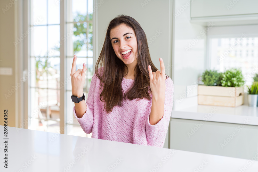 Beautiful young woman wearing pink sweater shouting with crazy expression doing rock symbol with hands up. Music star. Heavy concept. Beautiful young woman wearing pink sweater shouting with crazy expression doing rock symbol with hands up. Music star. Heavy concept.