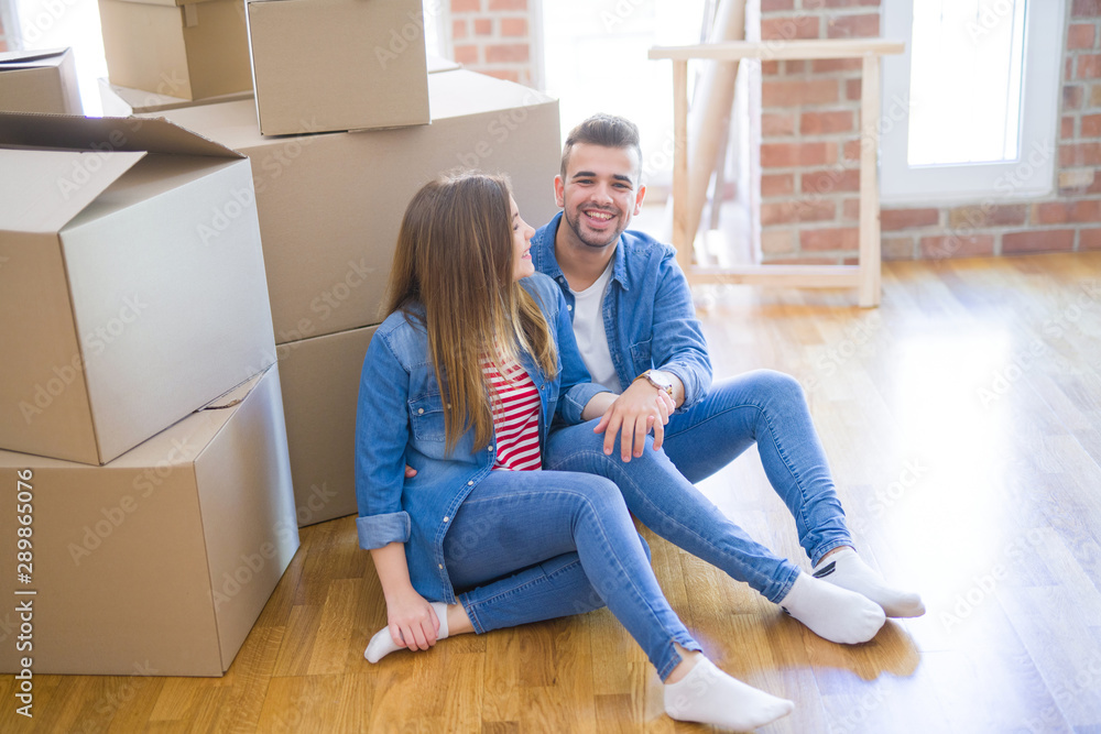 Young beautiful couple in love moving to new home, sitting on the floor very happy and cheerful for new apartment around cardboard boxes Young beautiful couple in love moving to new home, sitting on the floor very happy and cheerful for new apartment around cardboard boxes
