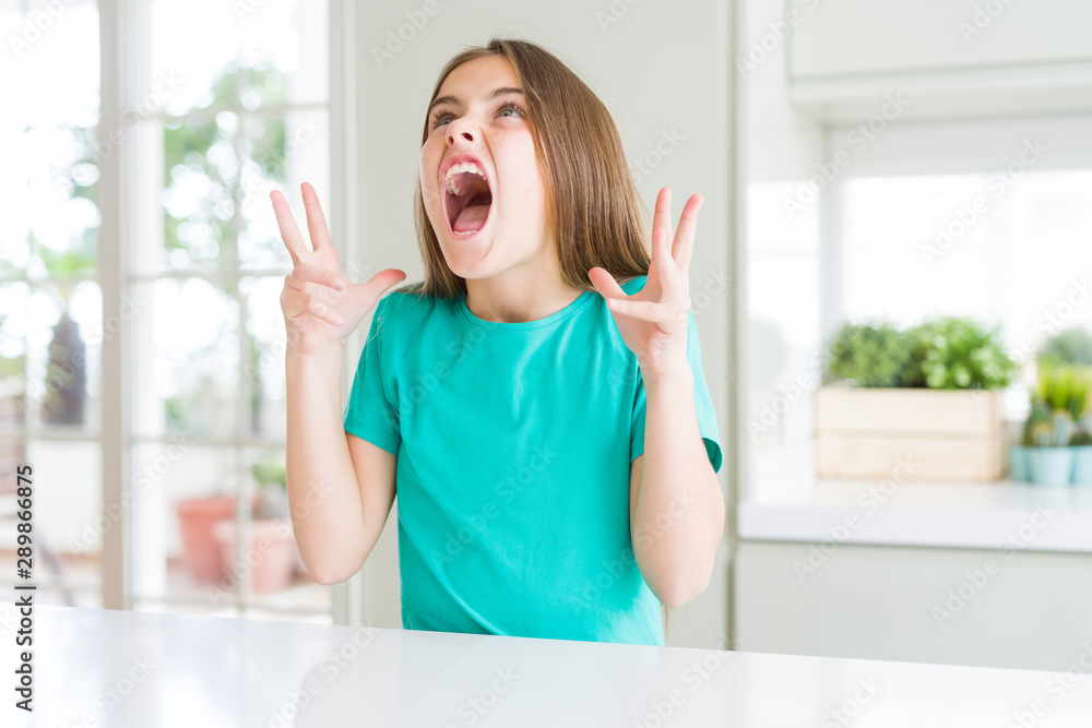 Beautiful young girl kid wearing green t-shirt crazy and mad shouting and yelling with aggressive expression and arms raised. Frustration concept. Beautiful young girl kid wearing green t-shirt crazy and mad shouting and yelling with aggressive expression and arms raised. Frustration concept.