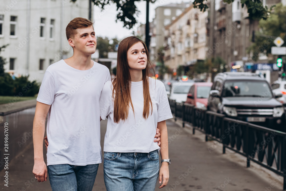 young couple walks the streets of the city and hold hands. guy and girl in white t-shirts and jeans outdoors. Teenagers walk in the autumn city. Happy young couple. young couple walks the streets of the city and hold hands. guy and girl in white t-shirts and jeans outdoors. Teenagers walk in the autumn city. Happy young couple.