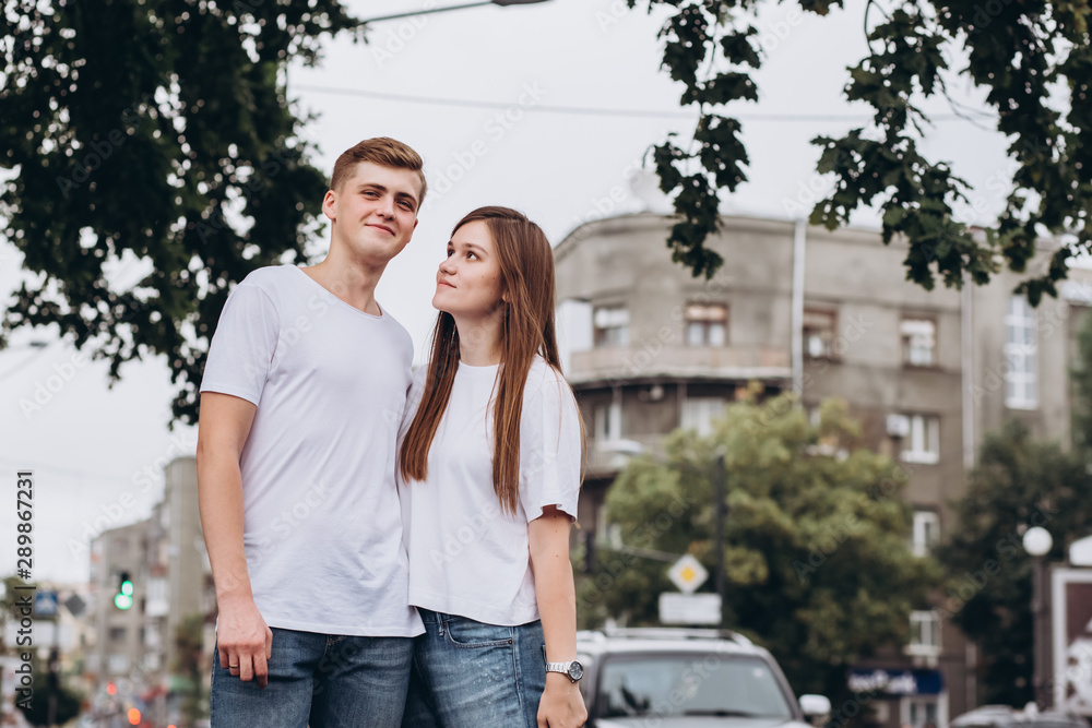 young couple walks the streets of the city and hold hands. guy and girl in white t-shirts and jeans outdoors. Teenagers walk in the autumn city. Happy young couple. young couple walks the streets of the city and hold hands. guy and girl in white t-shirts and jeans outdoors. Teenagers walk in the autumn city. Happy young couple.