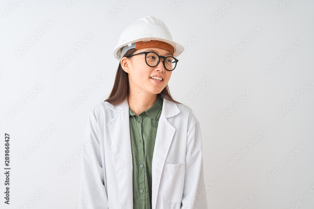 Young chinese engineer woman wearing coat helmet glasses over isolated white background looking away to side with smile on face, natural expression. Laughing confident. Young chinese engineer woman wearing coat helmet glasses over isolated white background looking away to side with smile on face, natural expression. Laughing confident.