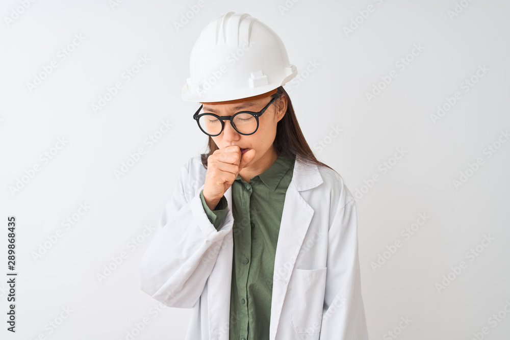 Young chinese engineer woman wearing coat helmet glasses over isolated white background feeling unwell and coughing as symptom for cold or bronchitis. Healthcare concept. Young chinese engineer woman wearing coat helmet glasses over isolated white background feeling unwell and coughing as symptom for cold or bronchitis. Healthcare concept.