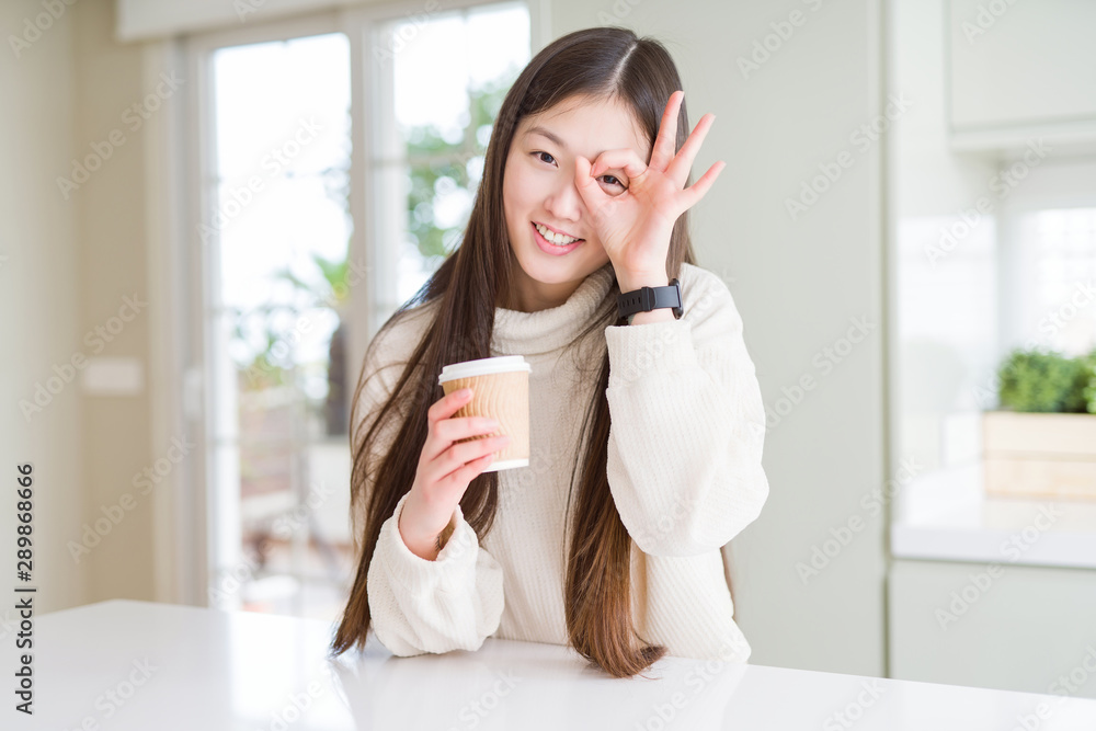Beautiful Asian woman drinking a coffee in a take away paper cup with happy face smiling doing ok sign with hand on eye looking through fingers Beautiful Asian woman drinking a coffee in a take away paper cup with happy face smiling doing ok sign with hand on eye looking through fingers