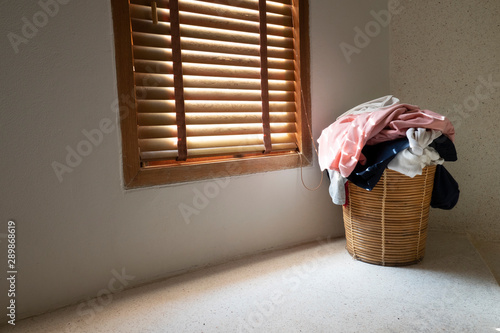 Heap of dirty clothes in wicker basket at corner in room near window are waiting to clean. photo