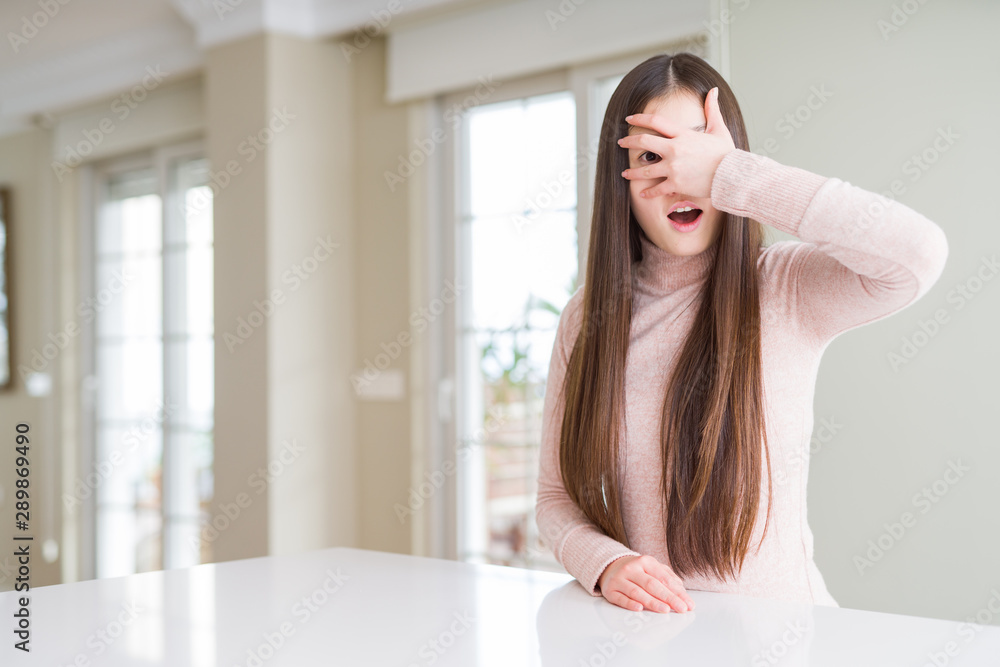 Beautiful Asian woman wearing casual sweater on white table peeking in shock covering face and eyes with hand, looking through fingers with embarrassed expression. Beautiful Asian woman wearing casual sweater on white table peeking in shock covering face and eyes with hand, looking through fingers with embarrassed expression.
