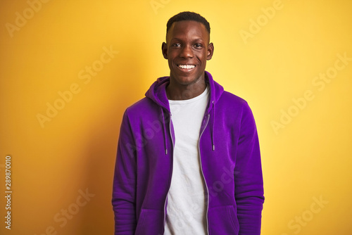 African american man wearing purple sweatshirt standing over isolated yellow background with a happy and cool smile on face. Lucky person.
