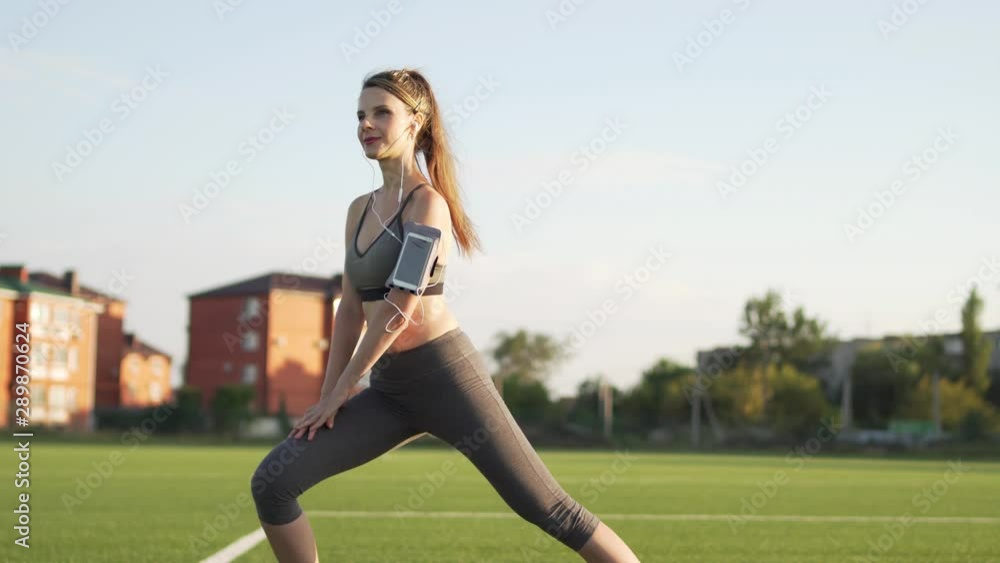 A slender runner is preparing for a morning jog to the music. A female runner is warming up and doing leg stretches in an outdoor gym. Healthy sports lifestyle. Weight loss A slender runner is preparing for a morning jog to the music. A female runner is warming up and doing leg stretches in an outdoor gym. Healthy sports lifestyle. Weight loss