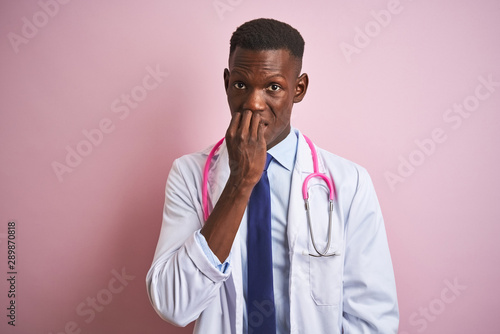 African american doctor man wearing stethoscope standing over isolated pink background looking stressed and nervous with hands on mouth biting nails. Anxiety problem.