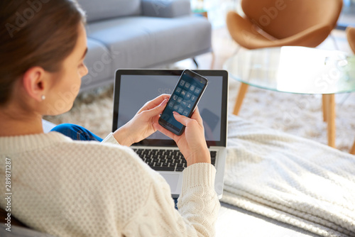 Woman text messaging on cell phone while sitting on sofa at home