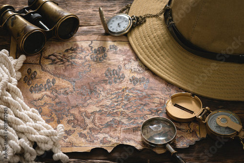 Old treasure map and adventure equipment on a wooden table background.