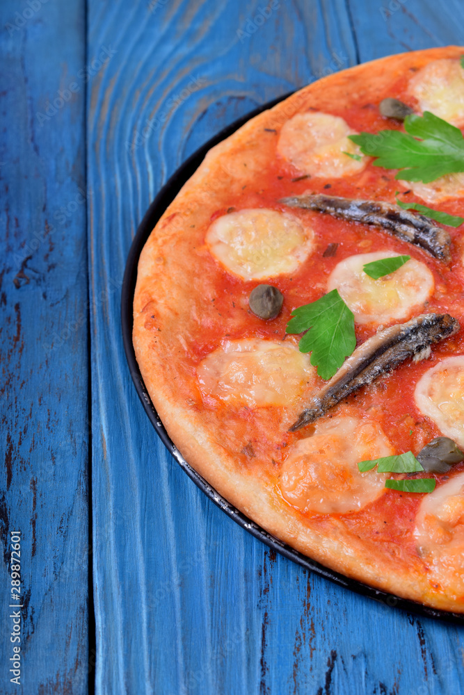 Round pizza with anchovies, capers, mozzarella cheese and tomato sauce garnished with fresh parsley
