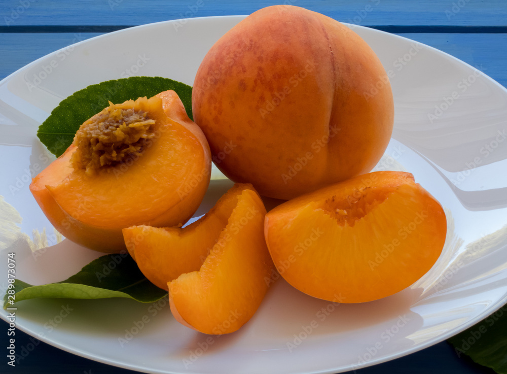 Yellow peaches full and cut on white plate, on blue table. Closeup, fruits