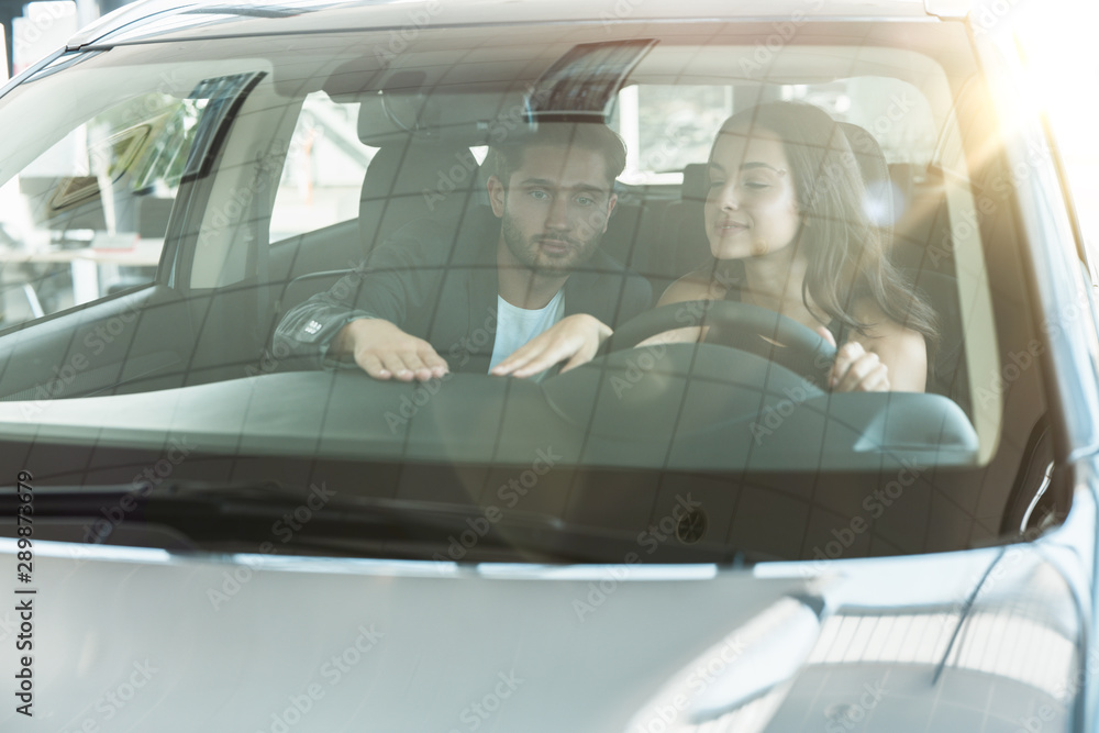 young couple handsome man and beautiful brunette woman looking for new car in dealership center young couple handsome man and beautiful brunette woman looking for new car in dealership center