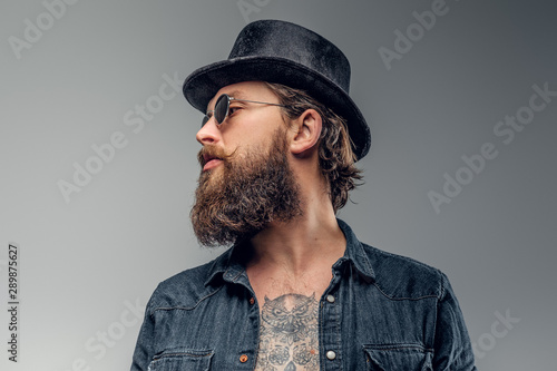 Serious bearded man in hat and sunglasses is posing at photo studio.