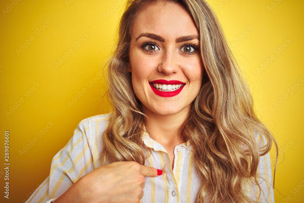 Young beautiful woman wearing stripes shirt standing over yellow isolated background with surprise face pointing finger to himself Young beautiful woman wearing stripes shirt standing over yellow isolated background with surprise face pointing finger to himself