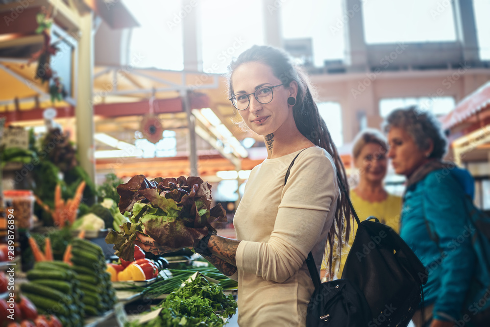 Young attractive woman with tattooes choosing fresh salad at vegetable market. Young attractive woman with tattooes choosing fresh salad at vegetable market.