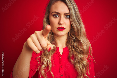 Young beautiful woman standing over red isolated background pointing with finger to the camera and to you  hand sign  positive and confident gesture from the front