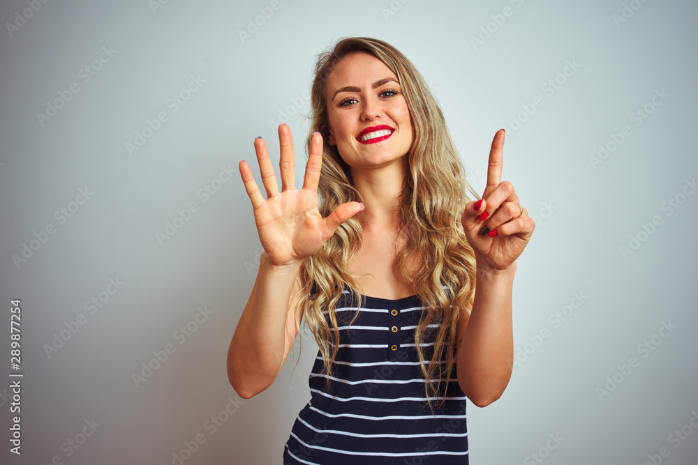 Young beautiful woman wearing stripes t-shirt standing over white isolated background showing and pointing up with fingers number six while smiling confident and happy. Young beautiful woman wearing stripes t-shirt standing over white isolated background showing and pointing up with fingers number six while smiling confident and happy.