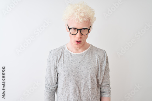 Young albino blond man wearing striped t-shirt and glasses over isolated white background afraid and shocked with surprise expression, fear and excited face.