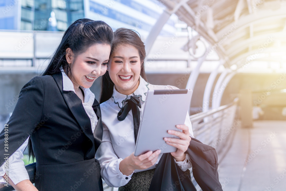 Two attractive Asian businesswomen checking on the tablet outdoors. Two attractive Asian businesswomen checking on the tablet outdoors.
