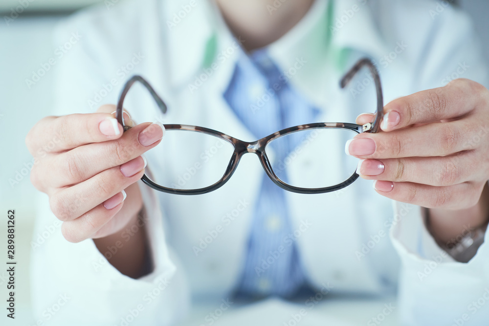 Female optician hands giving new glasses to customer for testing and trying close-up. Eye doctor with client comparing spectacles and choosing lenses in store. Female optician hands giving new glasses to customer for testing and trying close-up. Eye doctor with client comparing spectacles and choosing lenses in store.