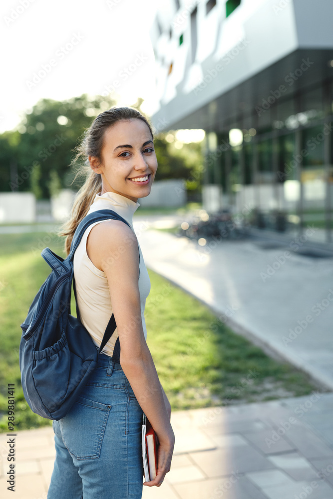 Beautiful happy woman with a backpack going to college. Young female university student with books in campus.