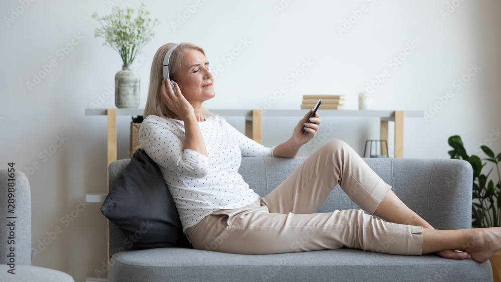 Mature woman in headphones enjoying favorite music, using phone Mature woman in headphones enjoying favorite music, using phone