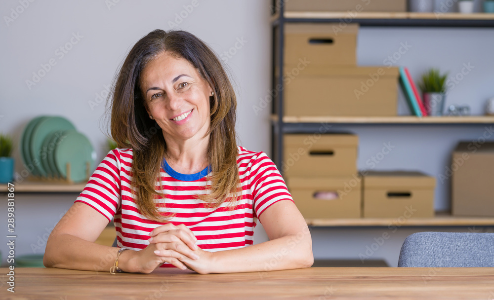 Middle age senior woman sitting at the table at home with hands together and crossed fingers smiling relaxed and cheerful. Success and optimistic Middle age senior woman sitting at the table at home with hands together and crossed fingers smiling relaxed and cheerful. Success and optimistic