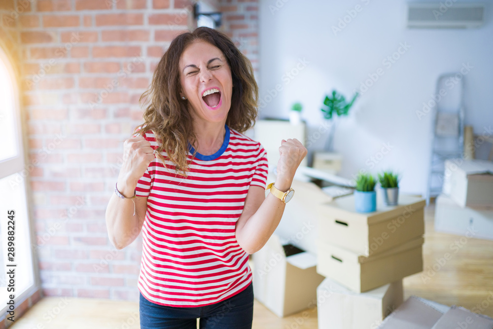 Middle age senior woman moving to a new house packing cardboard boxes very happy and excited doing winner gesture with arms raised, smiling and screaming for success. Celebration concept. Middle age senior woman moving to a new house packing cardboard boxes very happy and excited doing winner gesture with arms raised, smiling and screaming for success. Celebration concept.