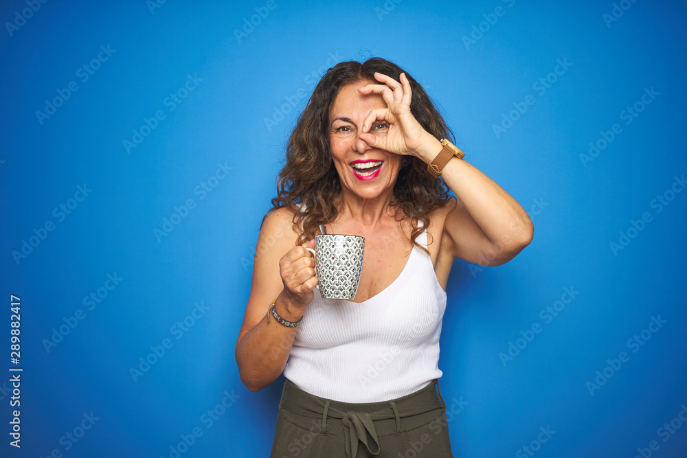 Middle age senior woman drinking a cup of coffee over blue isolated background with happy face smiling doing ok sign with hand on eye looking through fingers Middle age senior woman drinking a cup of coffee over blue isolated background with happy face smiling doing ok sign with hand on eye looking through fingers