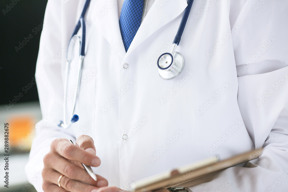 Close-up of clipboard with blank paper in medical doctor hand. Male doctor listens to the patient holding a clipboard with documents for hospitalization. Close-up of clipboard with blank paper in medical doctor hand. Male doctor listens to the patient holding a clipboard with documents for hospitalization.