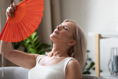 Exhausted older woman waving fan close up, suffering from heat photo
