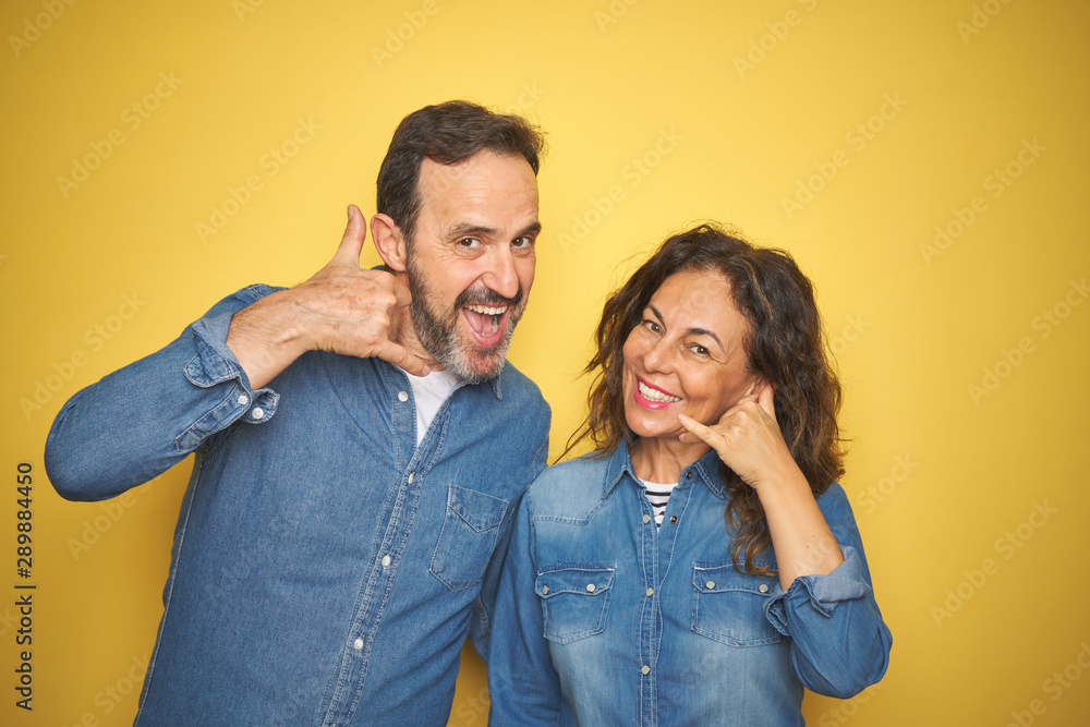 Fototapeta premium Beautiful middle age couple together standing over isolated yellow background smiling doing phone gesture with hand and fingers like talking on the telephone. Communicating concepts.