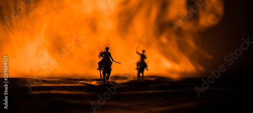 World war officer (or warrior) rider on horse with a sword ready to fight and soldiers on a dark foggy toned background. Battle scene battlefield of fighting soldiers. © zef art