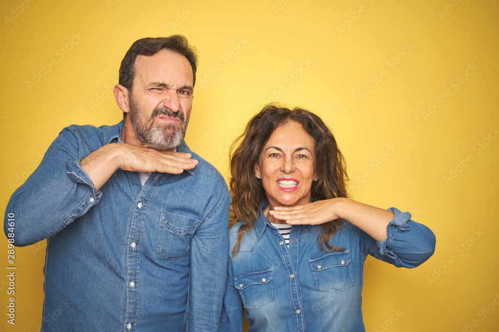 Beautiful middle age couple together standing over isolated yellow background cutting throat with hand as knife, threaten aggression with furious violence Beautiful middle age couple together standing over isolated yellow background cutting throat with hand as knife, threaten aggression with furious violence