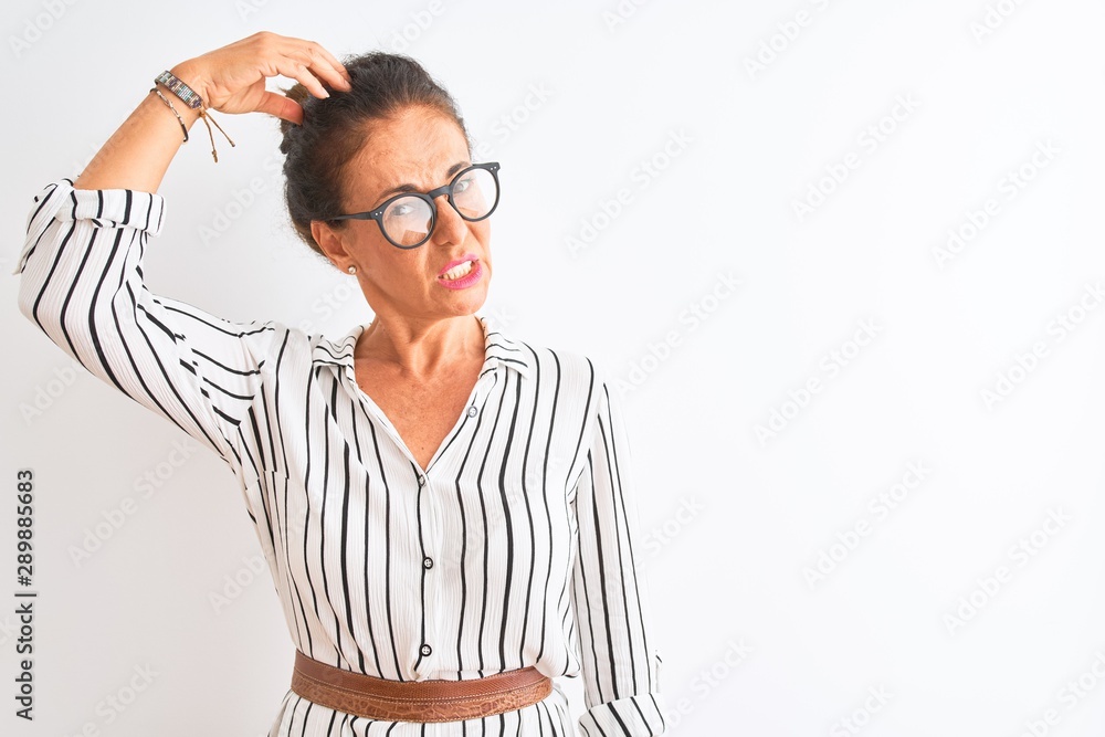 Middle age businesswoman wearing striped dress and glasses over isolated white background confuse and wondering about question. Uncertain with doubt, thinking with hand on head. Pensive concept. Middle age businesswoman wearing striped dress and glasses over isolated white background confuse and wondering about question. Uncertain with doubt, thinking with hand on head. Pensive concept.