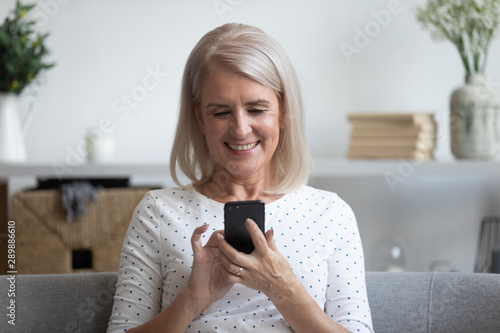 Smiling mature woman holding phone, using mobile device apps