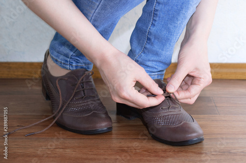 Caucasian girl tying shoelaces on brown shoes. Close-up.