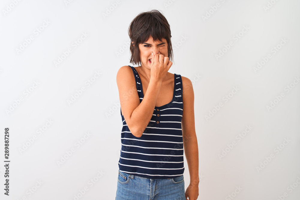 Young beautiful woman wearing striped t-shirt standing over isolated white background smelling something stinky and disgusting, intolerable smell, holding breath with fingers on nose. Bad smells Young beautiful woman wearing striped t-shirt standing over isolated white background smelling something stinky and disgusting, intolerable smell, holding breath with fingers on nose. Bad smells