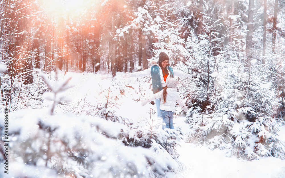 Naklejka premium Young family for a walk. Mom and daughter are walking in a winter park.